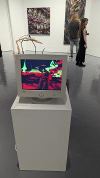 An image of a red, green, and blue artwork on a dated computer with people in the background looking at other artworks