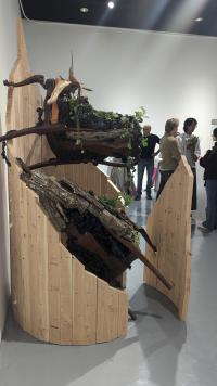 Image of an artwork made of a fooden frame and chairs that are covered in leaves